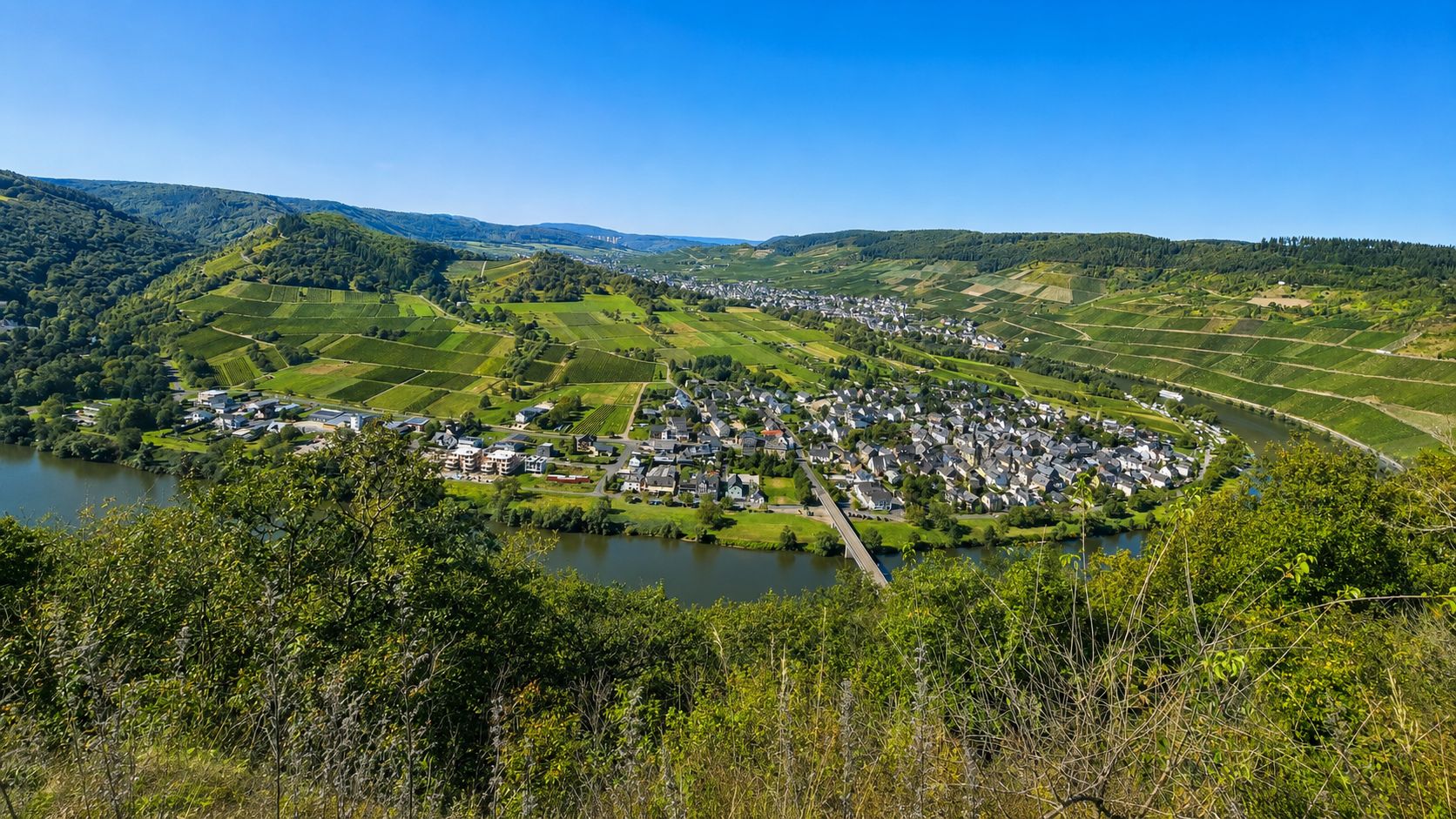A town with a river, surrounded by green fields and hills.