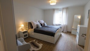 Ein modernes Schlafzimmer mit einem Bett, Nachttischen, einem Sessel, einem Spiegel und einem kleinen Kühlschrank.