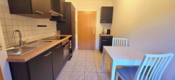 Cocina compacta con lavamanos, estufa y armarios, que da paso a un comedor con mesa y sillas.