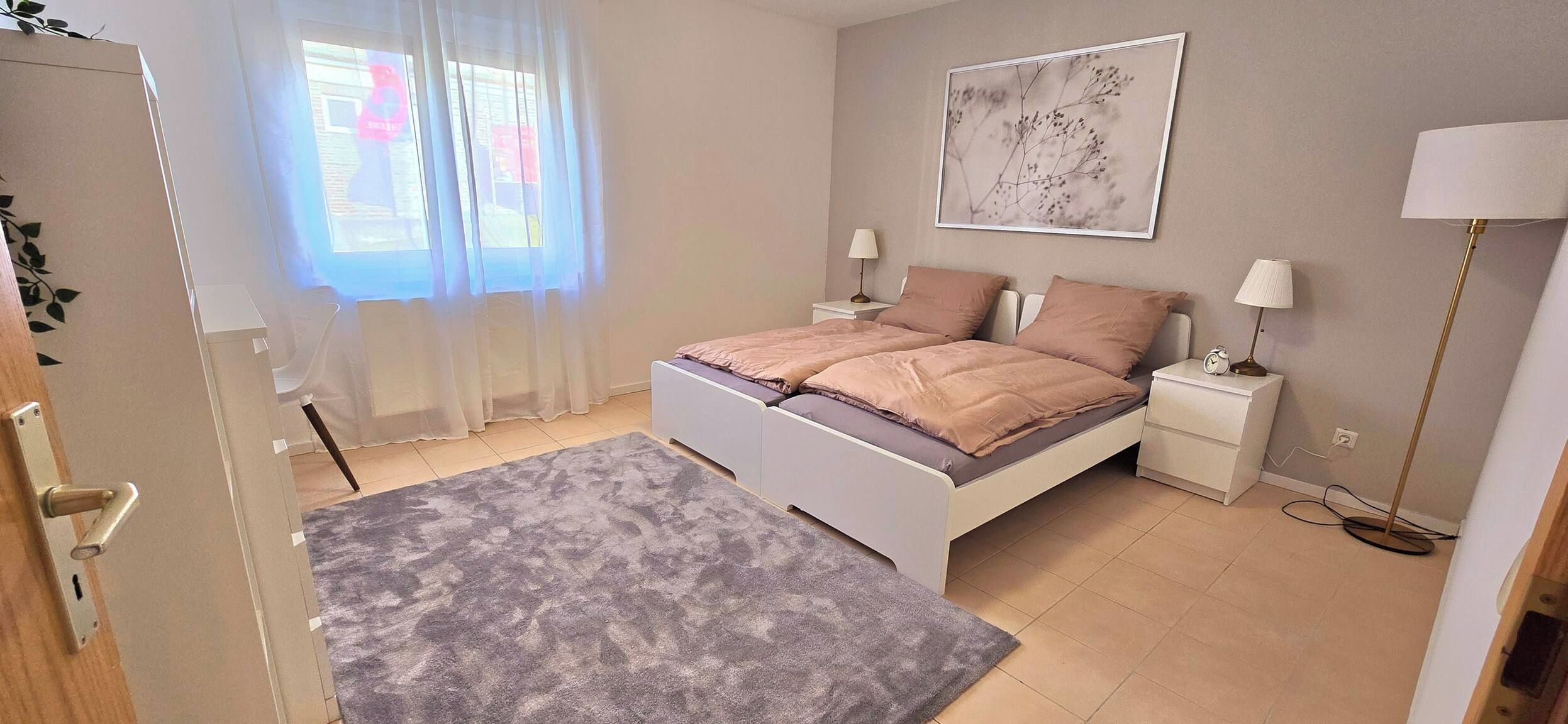 A bedroom with a bed, bedside tables, a lamp, a clock, and a window with curtains.