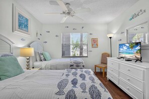 Quarto com cama, duas mesas de cabeceira, uma cadeira, cômoda, ventilador de teto e televisão.