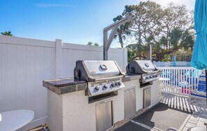 Ein Grillbereich im Freien mit weißem Zaun und Poolumgebung.