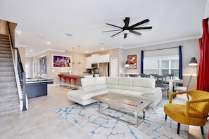 A modern living room with a sectional sofa, a coffee table, and a yellow armchair. - 4323 Scene | 5BR Waterview Townhome (Kissimmee)