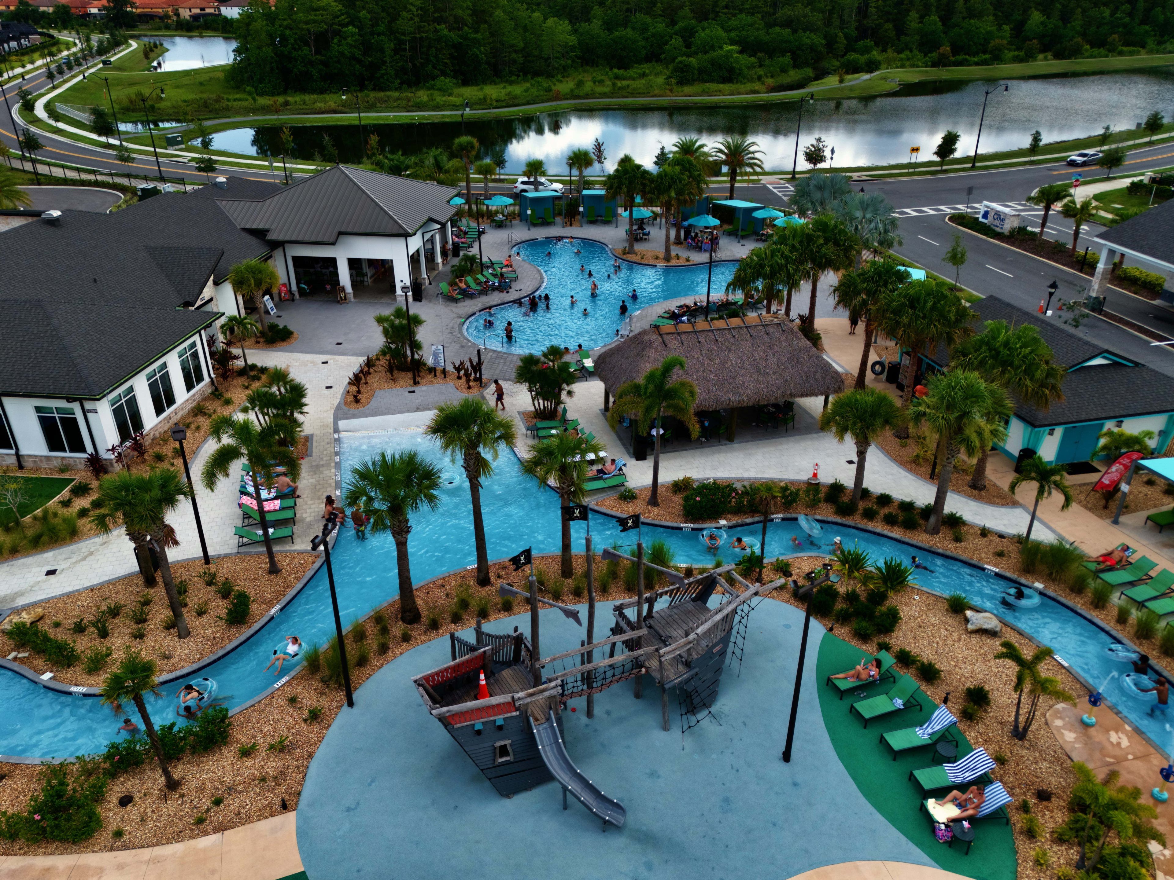 A large outdoor swimming pool area with multiple pools, palm trees, and a playground structure.