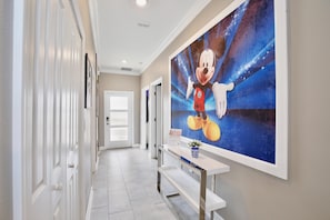 A hallway with a white door at the end, a bench, and a wall with a large cartoon character mural. - 4323 Scene | 5BR Waterview Townhome (Kissimmee)