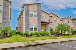 A multi-story residential building with a stone facade, large windows, and a well-maintained lawn with palm trees. - 4323 Scene | 5BR Waterview Townhome (Kissimmee)
