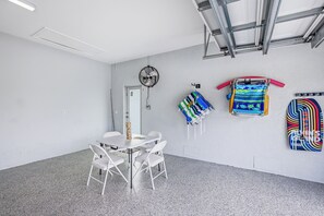 A room with a white table and chairs, a hanging fan, and colorful towels on the wall.