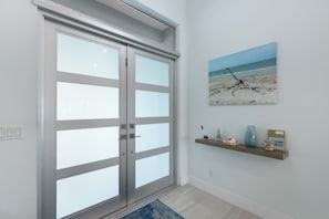 A modern interior with a sliding glass door, a beach-themed artwork, and a shelf with decorative items. - Serene Waterfront Bliss – Private Pool Home Near Beach Access, Sleeps 8 (Marco Island)