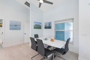 Un espace repas moderne avec une table blanche, des chaises noires et un ventilateur de plafond.