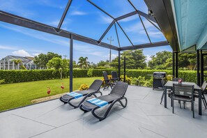A covered outdoor patio with lounge chairs, a grill, and a view of a well-maintained garden.