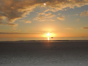 Une plage au coucher du soleil, un bateau sur l’eau et un ciel dégagé.