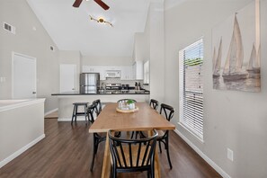 A modern kitchen with white cabinets, stainless steel appliances, and a dining area with a wooden table and black chairs. - Bombora, a Lake View Escape at April Sound. (Montgomery)