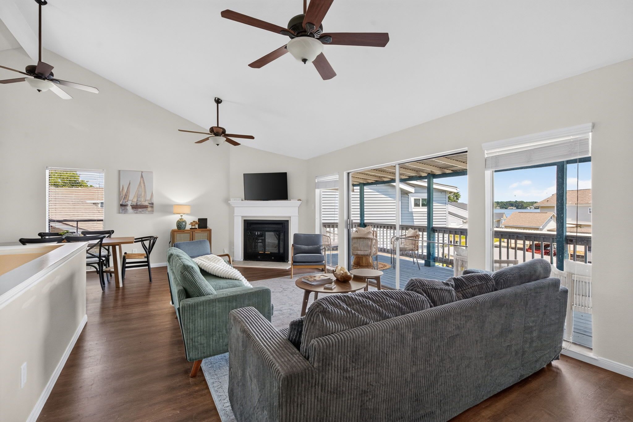 A spacious living room with a large gray sofa, a fireplace, and a balcony with a view of the water.