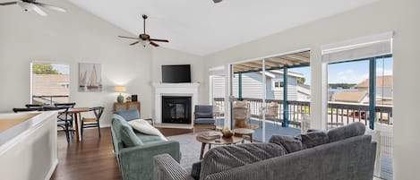 A spacious living room with a large gray sofa, a fireplace, and a balcony with a view of the water.