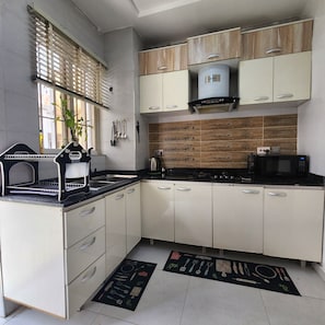 Una cocina con armarios blancos, encimera negra, microondas integrado y ventana con persianas.