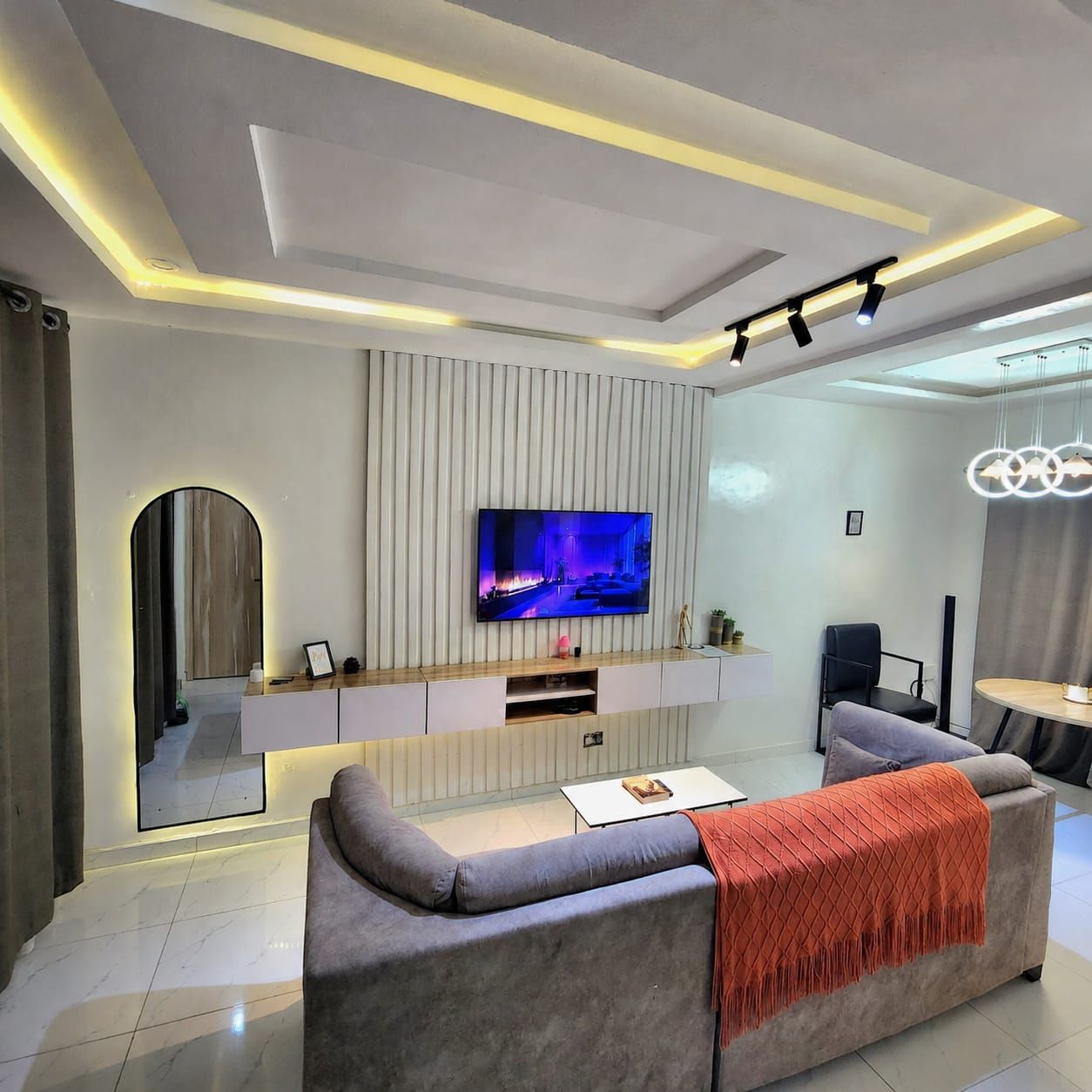 A modern living room with a flat-screen TV mounted on a wall, a sofa, a coffee table, and a dining area with a round table.