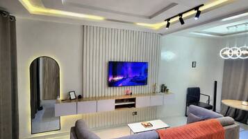A modern living room with a flat-screen TV mounted on a wall, a sofa, a coffee table, and a dining area with a round table.