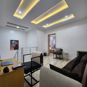 Una sala de estar moderna con un sofá, una pequeña mesa, una silla y un escritorio con una computadora portátil.