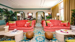 Um hall de hotel com dois sofás vermelhos, um tapete estampado e vista para a rua através de grandes janelas.