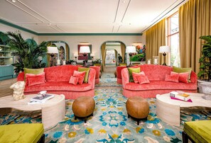 Un hall d’hôtel avec deux canapés rouges, une moquette à motifs et une vue sur la rue grâce à de grandes fenêtres.
