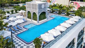 Uma piscina no terraço com espreguiçadeiras e guarda-sóis, rodeada por vegetação e um padrão de piso quadriculado.