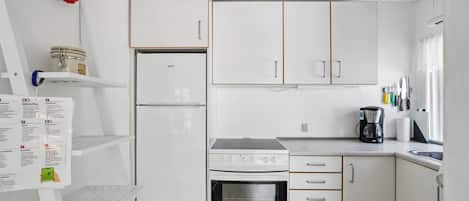 A compact kitchen with white cabinets, a refrigerator, a stove, and a coffee maker.