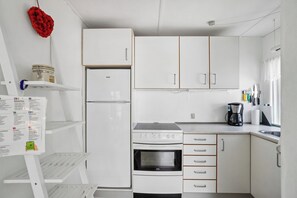 A compact kitchen with white cabinets, a refrigerator, a stove, and a coffee maker.