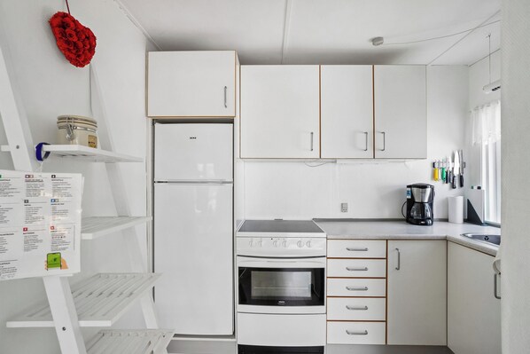 A compact kitchen with white cabinets, a refrigerator, a stove, and a coffee maker.