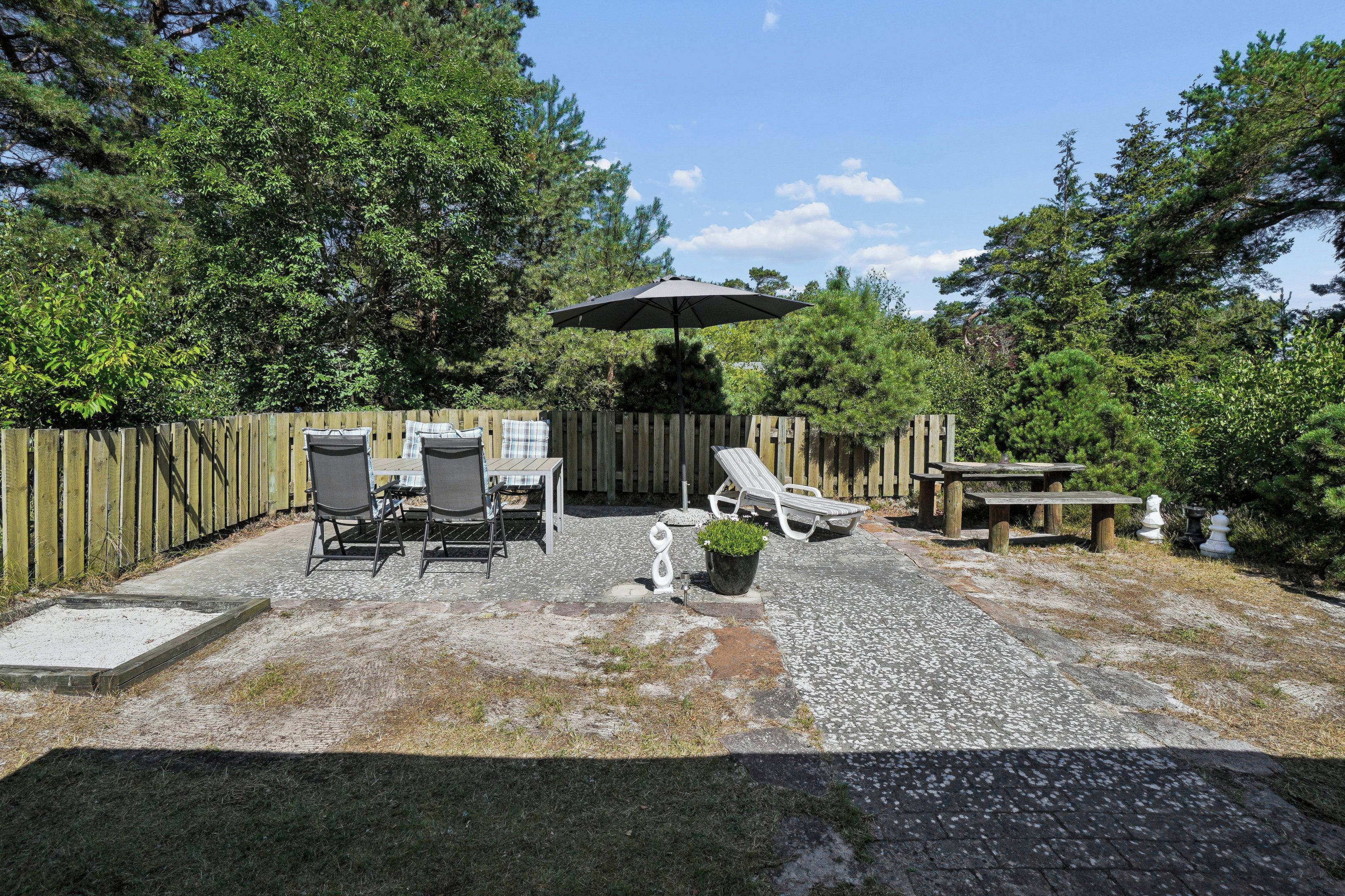 A patio with a table and chairs, a sun umbrella, and a wooden fence.