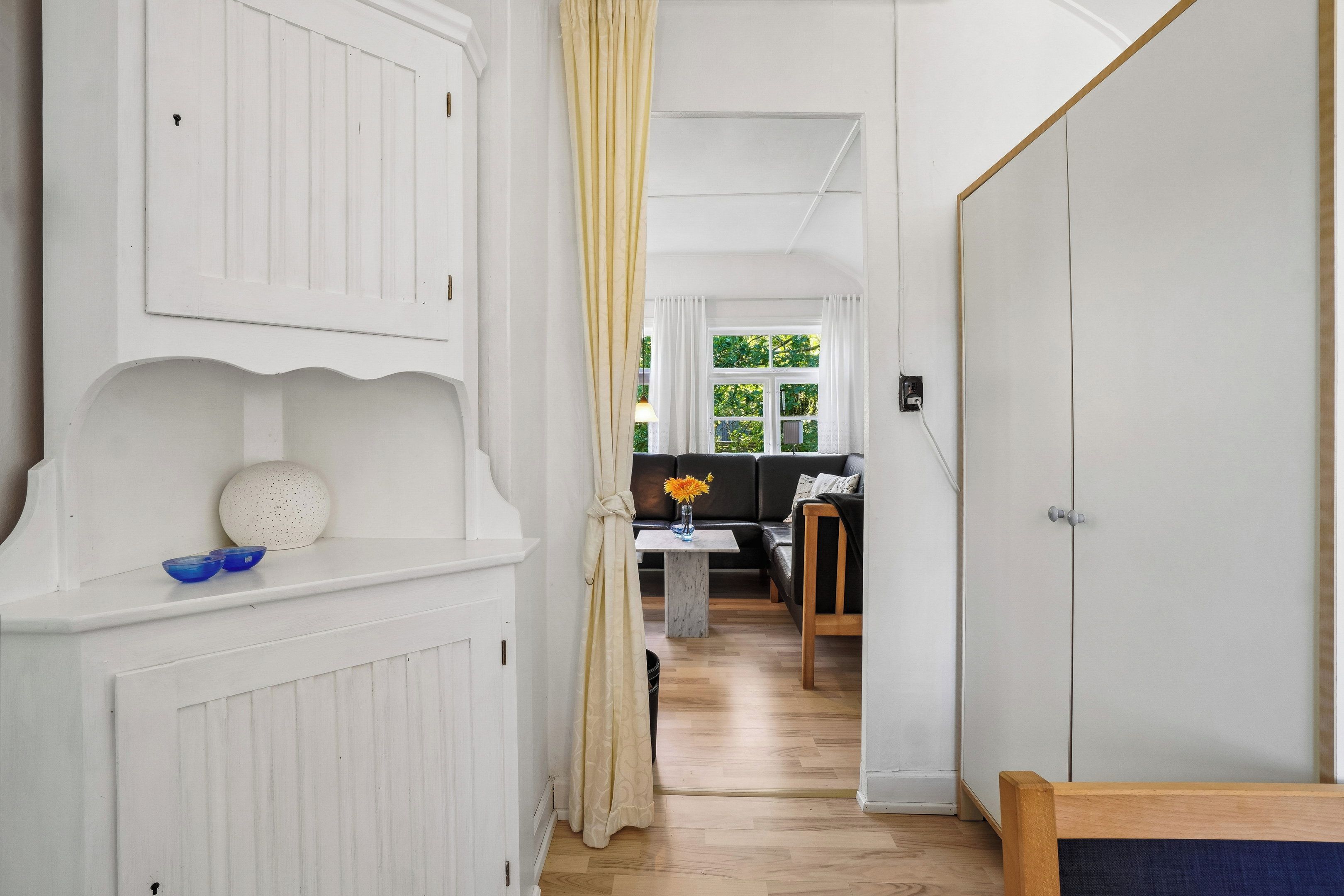 Un couloir aux murs blancs, avec un plancher en bois et une porte sur le côté droit.