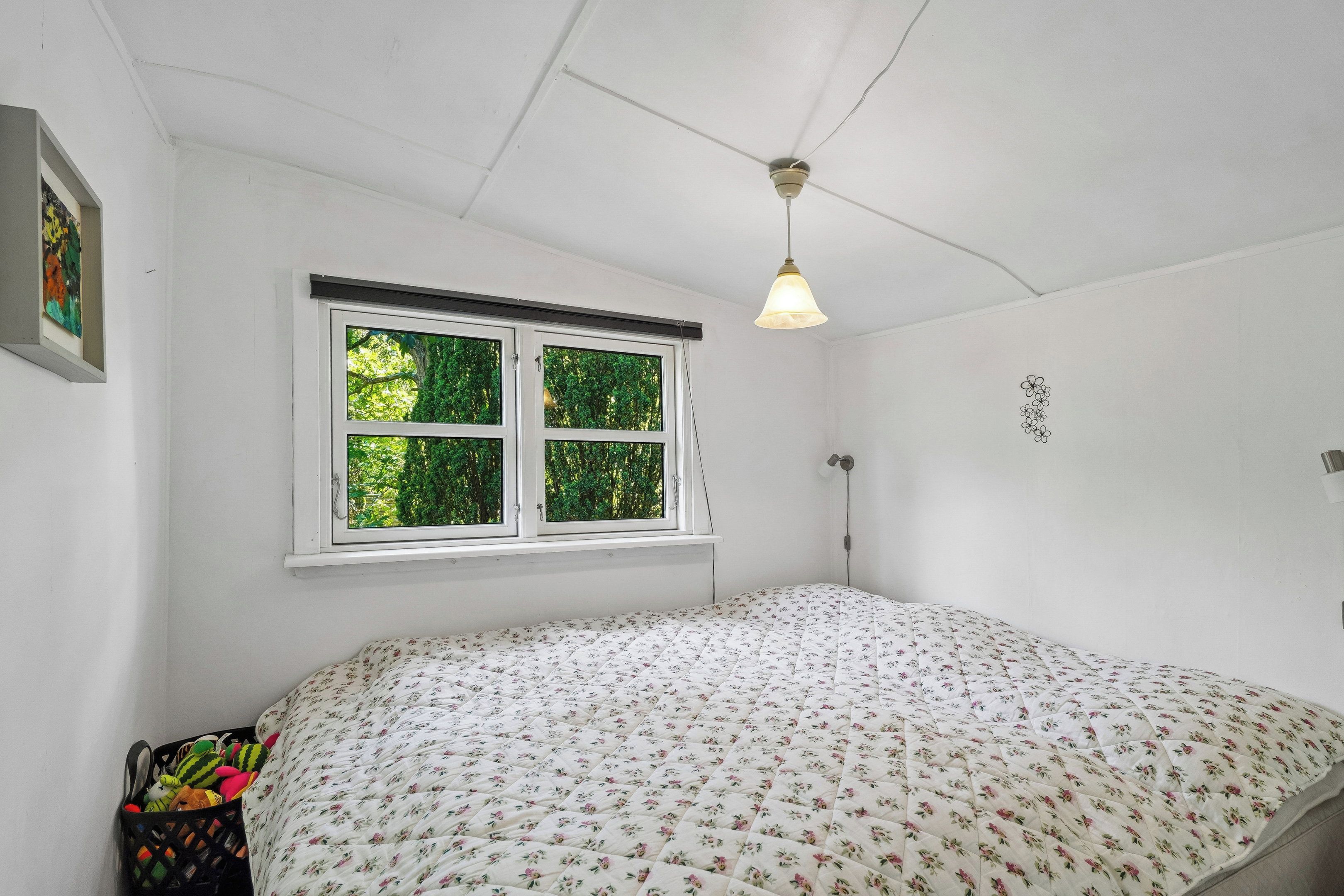 Une chambre à coucher avec un lit, une fenêtre avec des stores, un ventilateur de plafond et une lampe fixée au mur.
