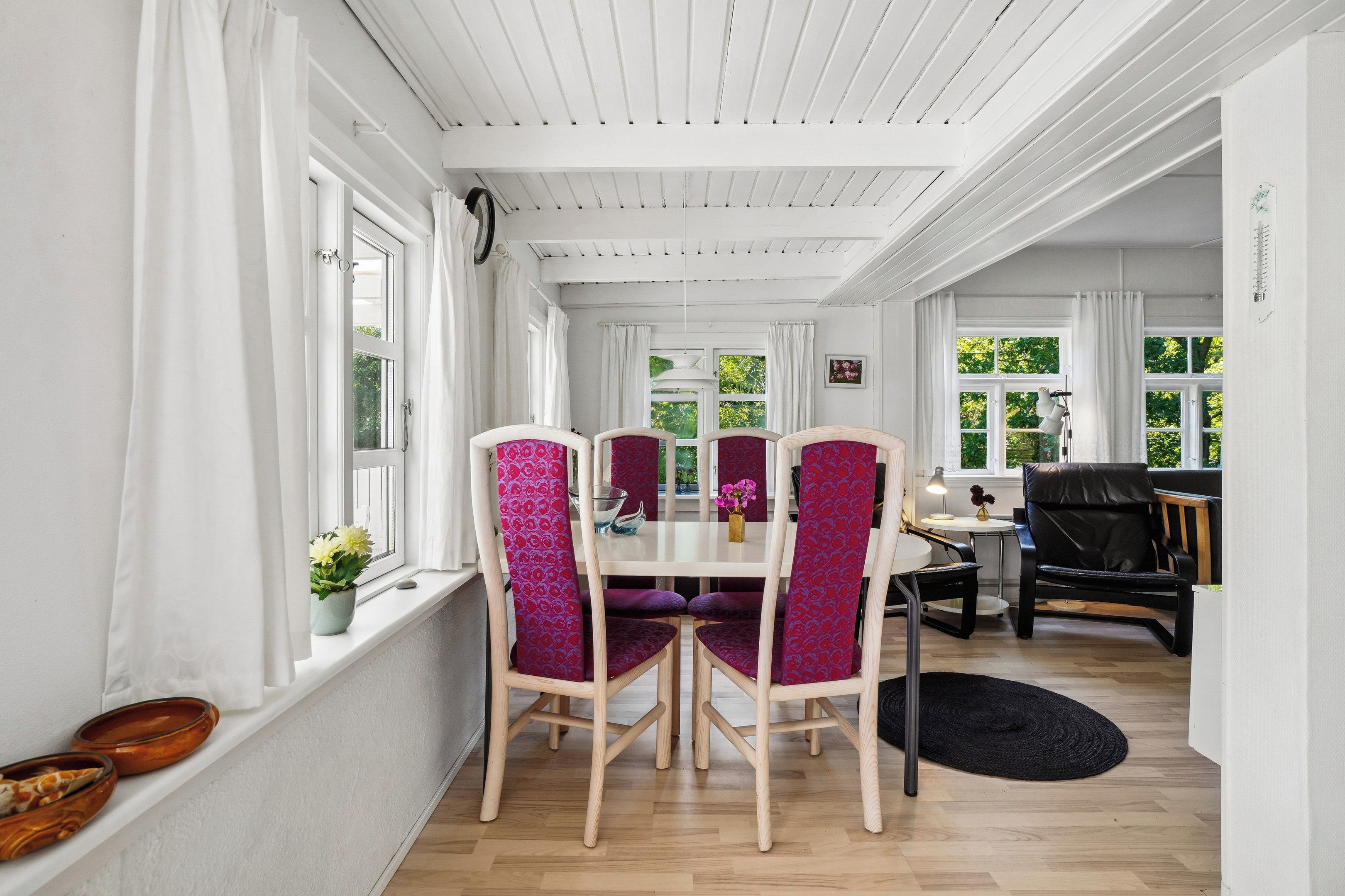 Een eethoek met een wit plafond, houten stoelen met een gestreept zitkussen, een ronde tafel en een zwart vloerkleed.