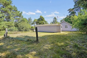 A small house with a fenced yard, surrounded by trees and a clear sky.