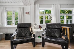 A room with two black leather chairs, a small round table with a vase of flowers, and a window with white curtains.