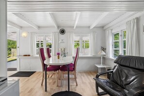 A room with a dining table, chairs, a sofa, and a window with curtains.