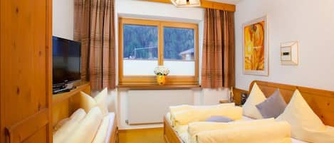 A hotel room with a bed, a television, a window with curtains, and a painting on the wall.