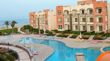 A resort pool area with a large pool, lounge chairs, and a building with balconies.
