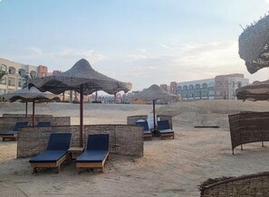 Une plage avec des chaises longues et des parasols en chaume.
