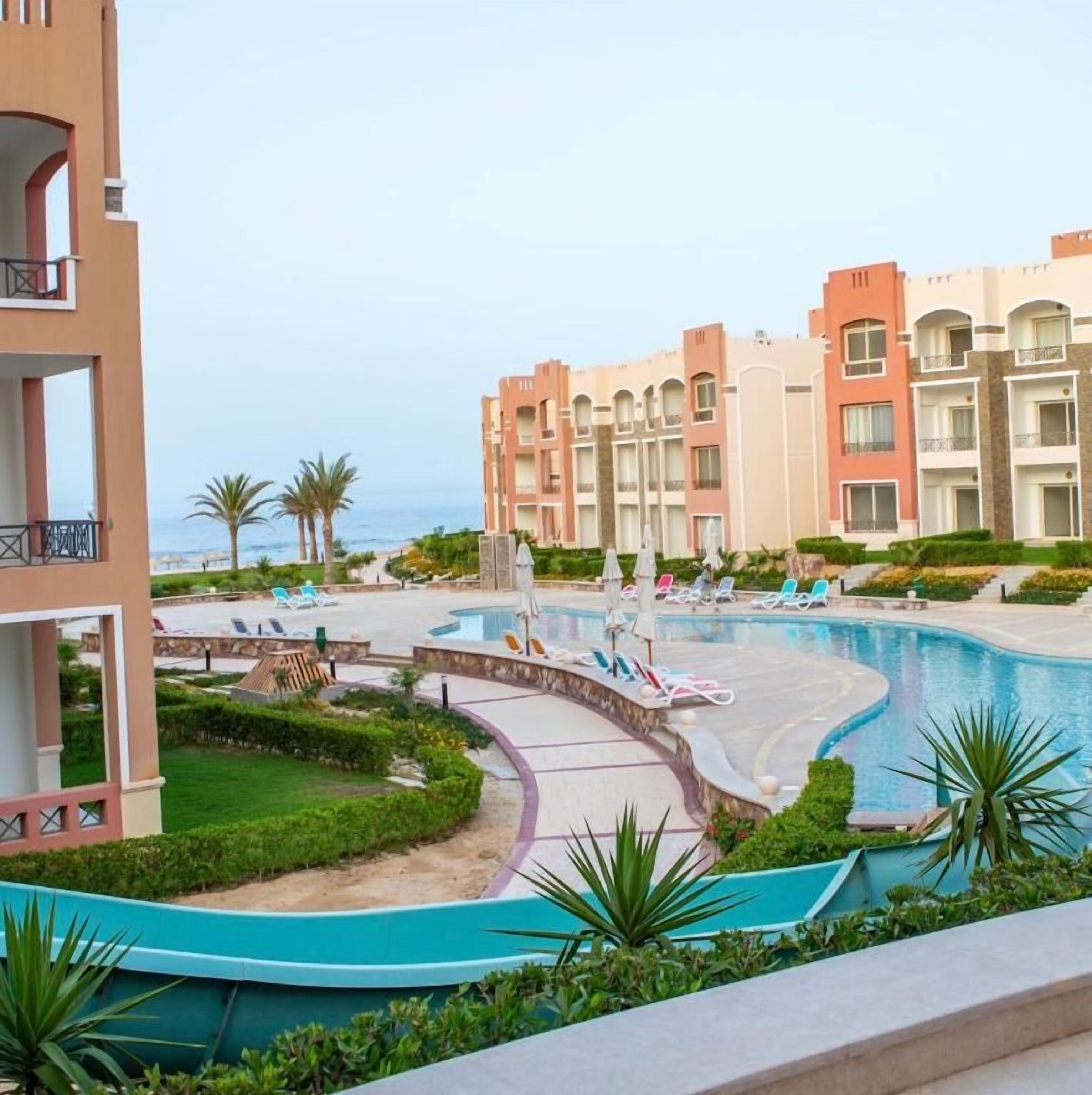 A resort with a swimming pool, lounge chairs, and a view of the sea.