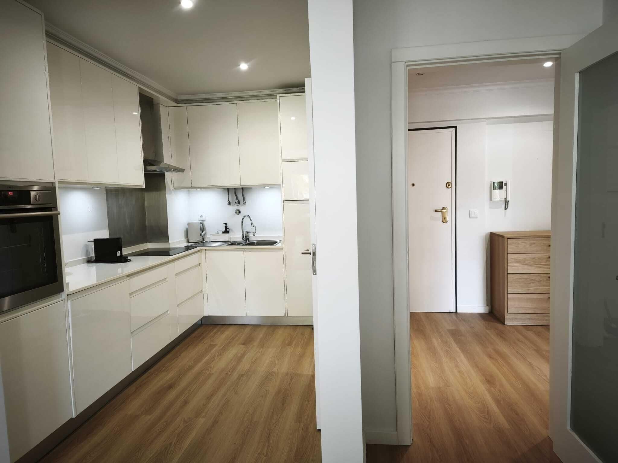 A modern kitchen with white cabinets, a stainless steel oven, and a wooden floor.