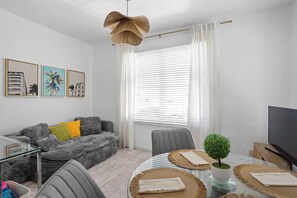 Una sala de estar moderna con un sofá, una mesa de comedor con posavasos, una planta pequeña en maceta y un televisor.