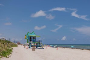 A lifeguard tower with a star-shaped roof, a beach with umbrellas, and a clear sky. - 100 Steps to the Sand - Art Deco Miami Beach Apartment (Miami)