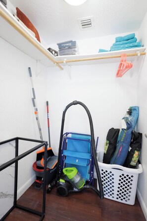 A storage area with a vacuum cleaner, a mop, and a laundry basket. - 100 Steps to the Sand - Art Deco Miami Beach Apartment (Miami)