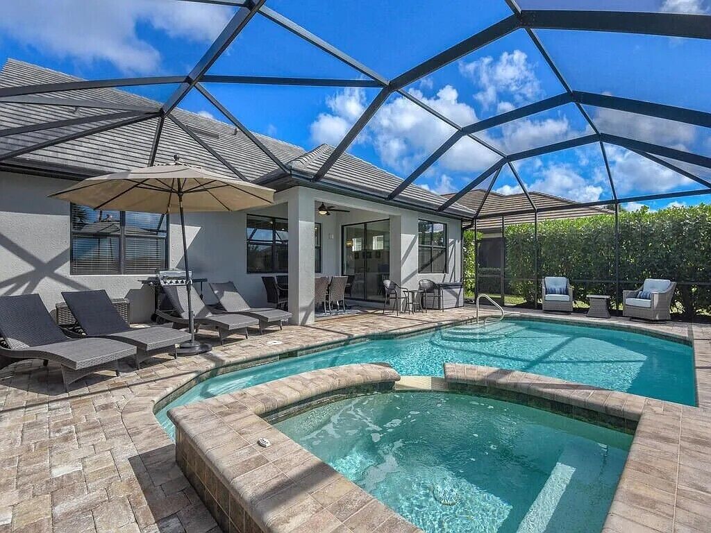 Une piscine entourée de chaises longues et de parasols, le tout bordé d’une terrasse couverte.