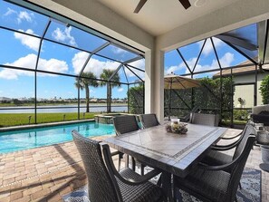 A poolside patio with a table and chairs, overlooking a body of water. - Resort-Style Naples Living in Winding Cypress- Private Pool, Spa & Waterfront (Naples)