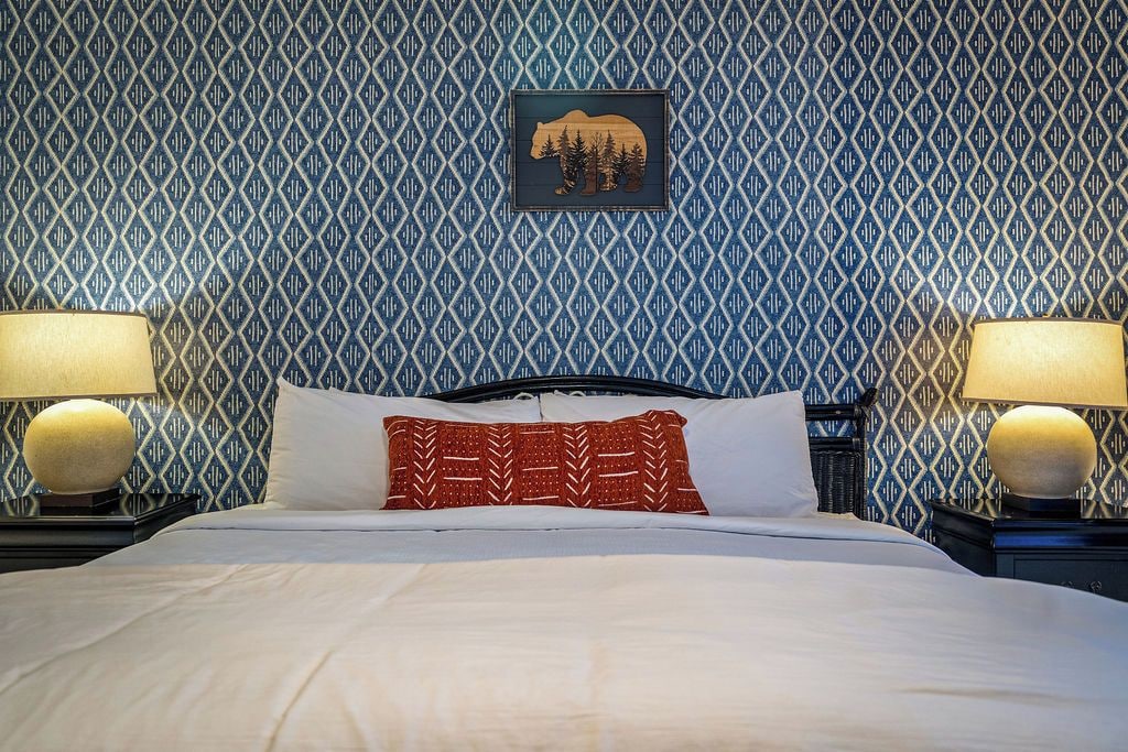 Una habitación de hotel con papel tapiz estampado, una cama con ropa blanca y dos lámparas de noche.