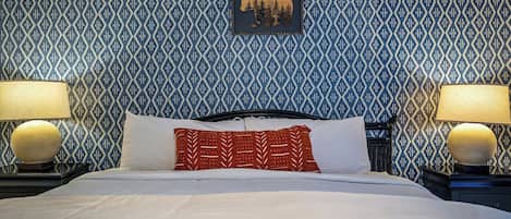 Una habitación de hotel con papel tapiz estampado, una cama con ropa blanca y dos lámparas de noche.