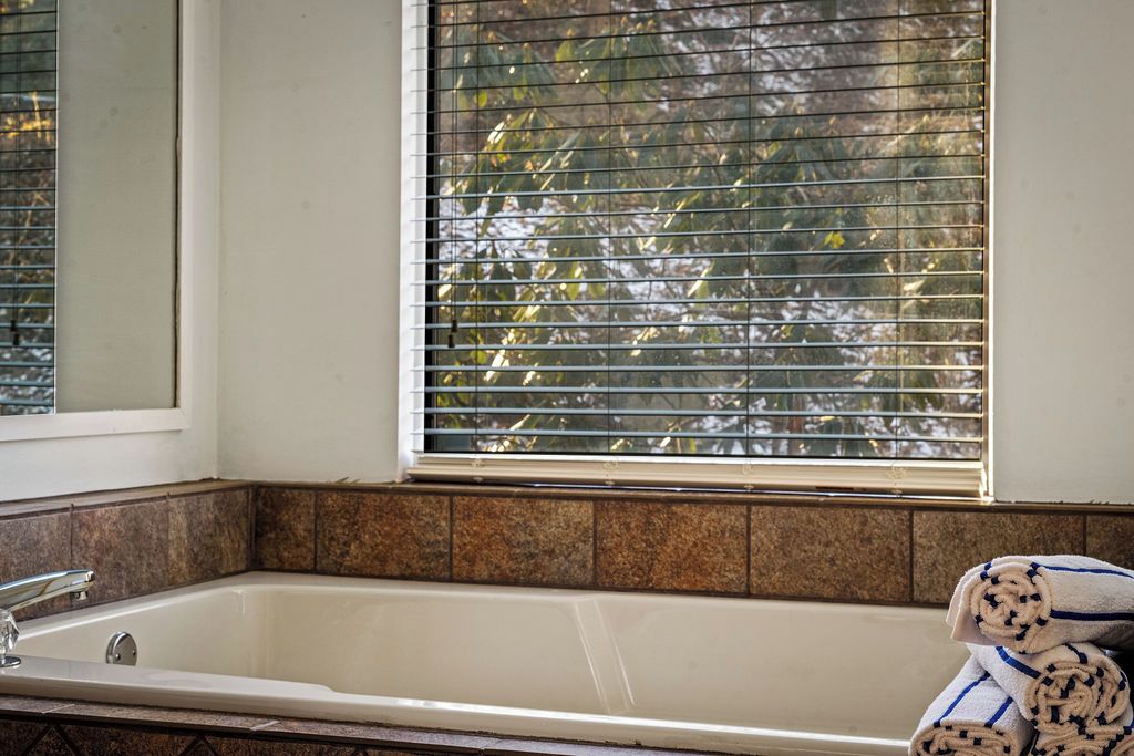 Ein Badezimmer mit einer Badewanne, einem Fenster mit Jalousien und einem Handtuchhalter mit Handtüchern.