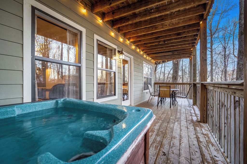 Une terrasse en bois avec un jacuzzi, des sièges d’extérieur et un espace abrité agrémenté de guirlandes lumineuses.