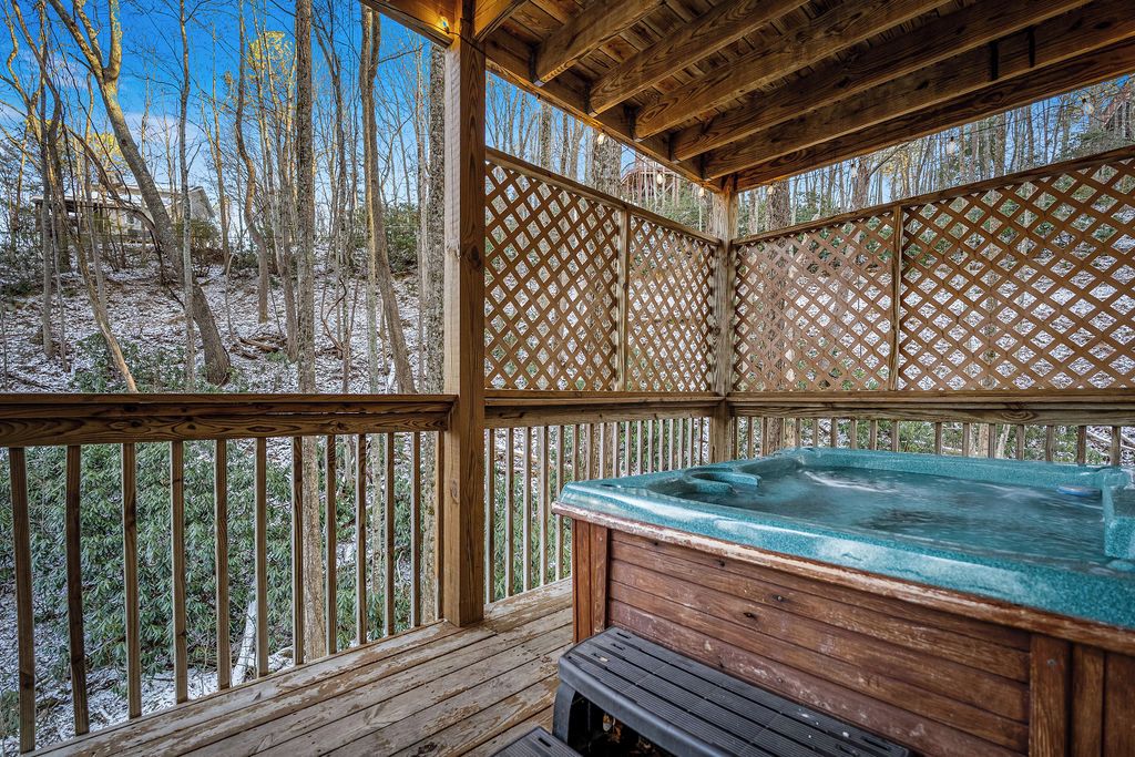 A wooden deck with a hot tub and a bench, surrounded by a lattice fence.
